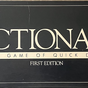 May include: Black rectangular box with the word "PICTIONARY" in large, white, serif font. Below, the text reads "THE GAME OF QUICK DRAW" and "FIRST EDITION" in a smaller, white font. The box has a white border.