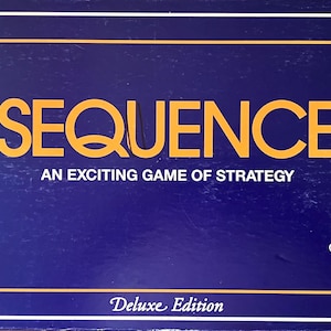 May include: A rectangular board game box with a deep blue background and a gold border. The text reads SEQUENCE, AN EXCITING GAME OF STRATEGY, and Deluxe Edition. A small white rectangular graphic in the corner features the signature of Bill Barrett.