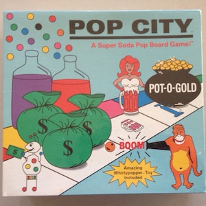 May include: A colorful board game box for Pop City, a Super Soda Pop Board Game. The box features a cartoon illustration of a woman with red hair, a pot of gold, and a monkey. The game includes a Whirlypopper toy.