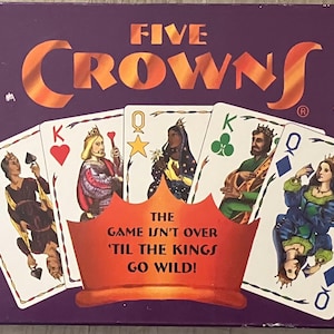 Puede incluir: Una caja del juego de cartas Five Crowns con un fondo morado y el t&iacute;tulo del juego en naranja. La caja presenta naipes con reyes y reinas. El texto en la caja incluye "2-7 jugadores" y "Edades 8-Adultos."