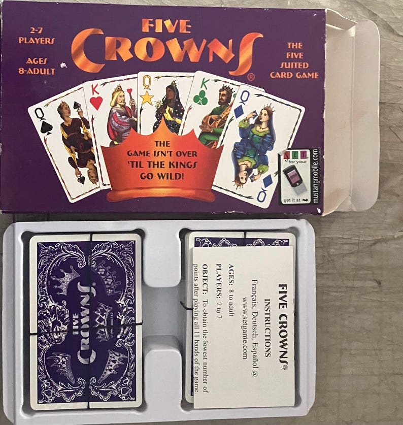 Puede incluir: Una caja del juego de cartas Five Crowns con un fondo morado y el t&iacute;tulo del juego en naranja. La caja muestra naipes con reyes y reinas. El juego es para 2-7 jugadores, a partir de 8 a&ntilde;os. Las instrucciones del juego tambi&eacute;n son visibles.