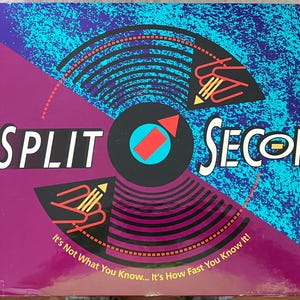 May include: A board game box with the title "SPLIT SECOND" in white letters. The design features a black circle with a red arrow, a blue and purple background, and the text "It's Not What You Know... It's How Fast You Know It!"