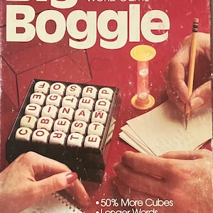 May include: A Big Boggle word game box featuring a red background with white text that reads Big Boggle, Parker Brothers, Bigger Hidden WORD Game, 50% More Cubes, Longer Words, Greater Challenge, and See box bottom for details. Includes letter cubes.