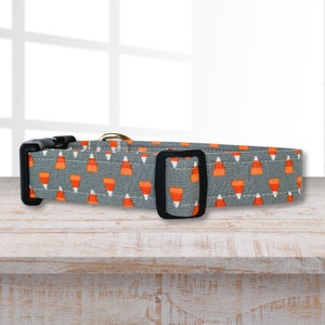 Puede incluir: Un collar de perro gris con un patrón de maíz dulce naranja y blanco. El collar tiene una hebilla negra.