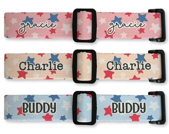 Op de afbeelding: Drie gepersonaliseerde hondenhalsbanden met zwarte gespen. De bovenste halsband is roze met witte, rode en blauwe sterren en de naam "Gracie". De middelste halsband is beige met de naam "Charlie". De onderste halsband is lichtblauw met de naam "Buddy".