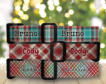 Puede incluir: Collares para perros con patrones de cuadros rojos, verdes y azules. Cada collar tiene una hebilla negra y presenta un nombre: "Bruno", "Cody" y "Charlie". Los collares se muestran sobre una superficie de madera con un fondo borroso de luces navideñas.