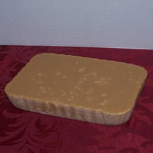 Puede incluir: Un bloque rectangular de caramelo de color marr&oacute;n claro con una textura ligeramente rugosa. El caramelo est&aacute; sobre una superficie roja con estampado.