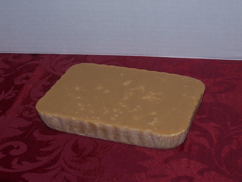 Puede incluir: Un bloque rectangular de caramelo de color marr&oacute;n claro con una textura ligeramente rugosa. El caramelo est&aacute; sobre una superficie roja con estampado.