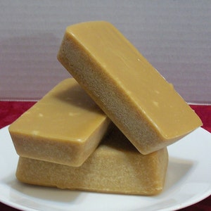 Puede incluir: Tres bloques rectangulares de caramelo marr&oacute;n claro apilados uno encima del otro en un plato blanco.