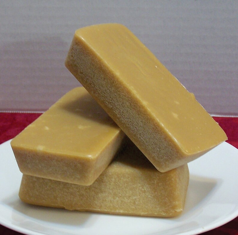 Puede incluir: Tres bloques rectangulares de caramelo marr&oacute;n claro apilados uno encima del otro en un plato blanco.