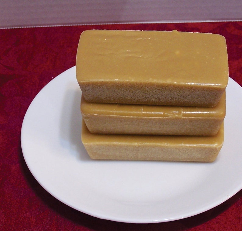 Puede incluir: Tres bloques rectangulares de fudge marr&oacute;n claro apilados en un plato blanco. El fudge es liso y brillante.