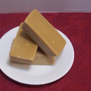 Puede incluir: Dos bloques rectangulares de fudge, uno encima del otro, en un plato blanco. El fudge es de color marr&oacute;n claro.