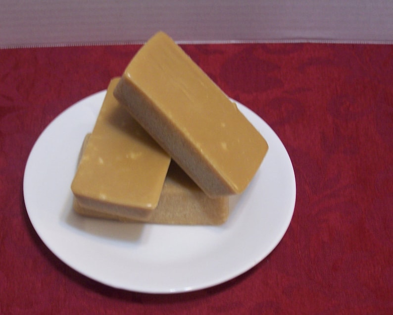 Puede incluir: Dos bloques rectangulares de fudge, uno encima del otro, en un plato blanco. El fudge es de color marr&oacute;n claro.