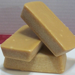 Puede incluir: Tres barras rectangulares de caramelo marr&oacute;n claro apiladas en un plato blanco.