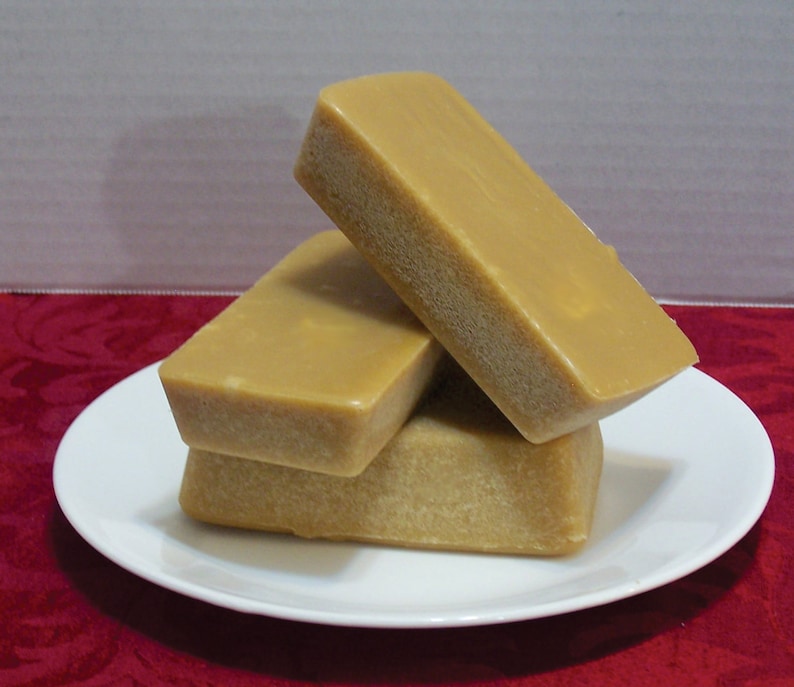 Puede incluir: Tres barras rectangulares de caramelo fudge apiladas en un plato blanco. El fudge es de color marr&oacute;n claro y tiene una superficie lisa y brillante.