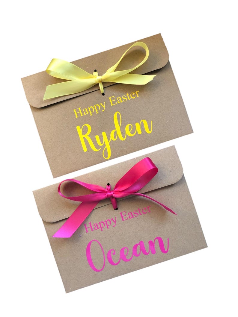 K&ouml;nnte beinhalten: Zwei Geschenk-Umschl&auml;ge aus Kraftpapier mit gelben und rosa B&auml;ndern. Der gelbe Umschlag tr&auml;gt den Text "Happy Easter Ryden". Der rosa Umschlag tr&auml;gt den Text "Happy Easter Ocean".