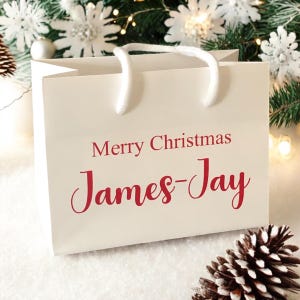 May include: White gift bag with red text that says "Merry Christmas James-Jay".