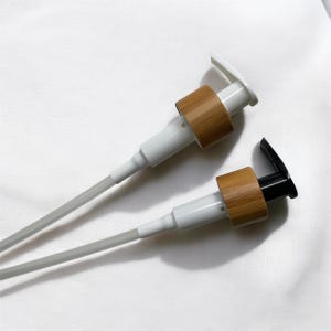May include: Two plastic pump bottles with clear tubes and wooden tops. One bottle has a white top and the other has a black top.