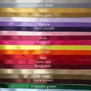 May include: A collection of colorful ribbons in various shades, including white, black, gold, purple, pink, red, and blue. Each ribbon is labeled with its color name in white text. The ribbons are arranged horizontally, showcasing a wide range of hues.