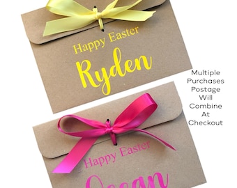 May include: Two brown paper gift bags with yellow and pink text that reads "Happy Easter" and names "Ryden" and "Ocean". Each bag is tied with a matching colored ribbon bow. The bags are on a white background.