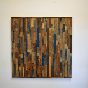 Op de afbeelding: Een wandkunstwerk gemaakt van gerecycled hout met verschillende houttinten en blauwe verfaccenten.