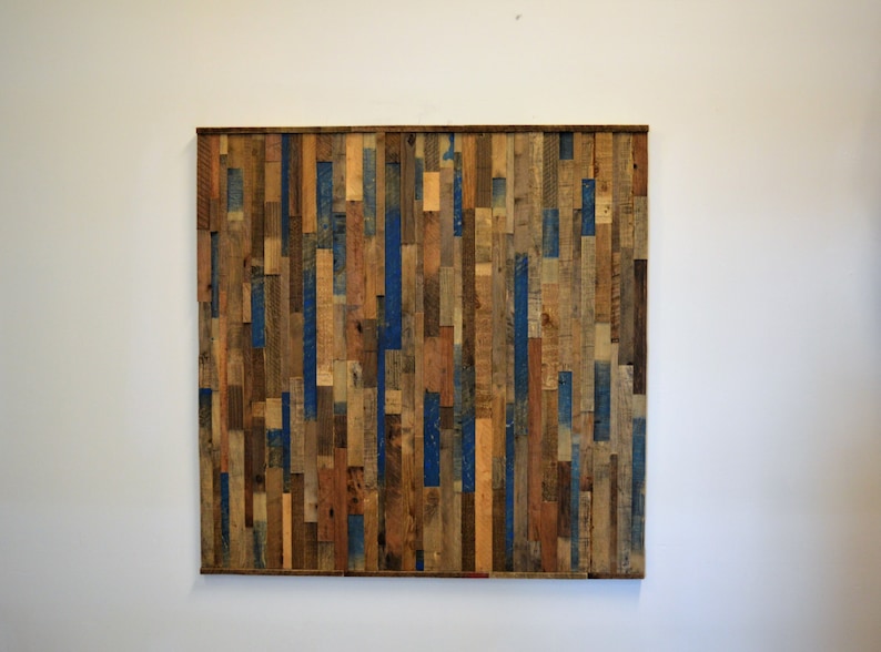 Op de afbeelding: Een wandkunstwerk gemaakt van gerecycled hout met verschillende houttinten en blauwe verfaccenten.
