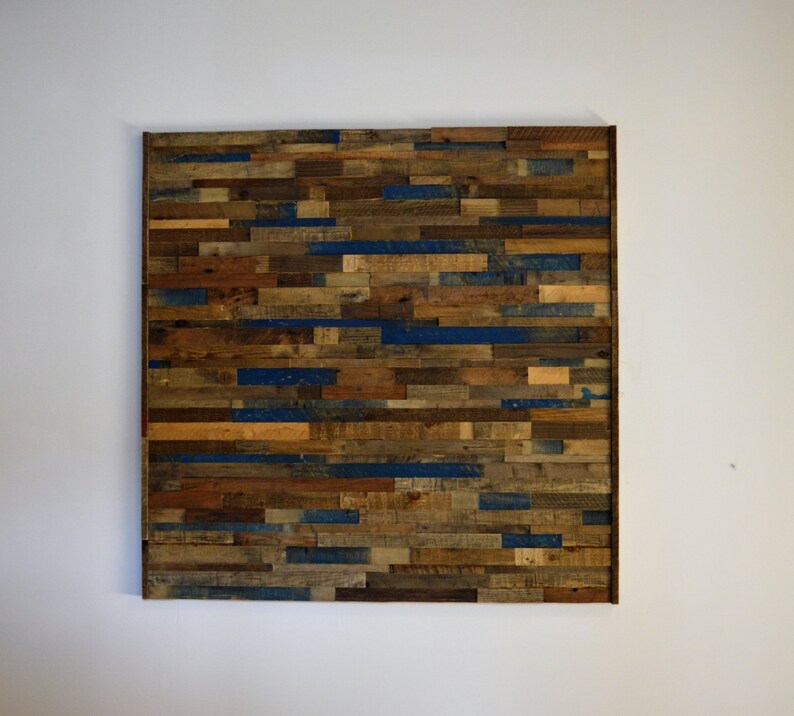 Op de afbeelding: Een wandkunstwerk gemaakt van gerecycled hout met een rustieke uitstraling. Het hout is in een horizontaal patroon gerangschikt en geschilderd in tinten bruin, blauw en beige.