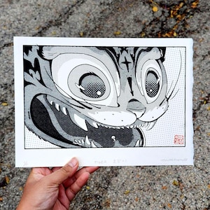 May include: Black and white print of a tiger's face with large eyes and sharp teeth. The artwork has a comic book style with halftone dots and the word "TIGER" in the bottom left corner.