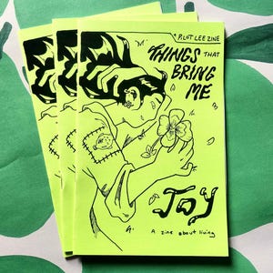 May include: A stack of three zines with a bright yellow cover. The cover features a black and white illustration of a person holding a flower. The title of the zine is "Things That Bring Me Joy" and the subtitle is "A zine about living."