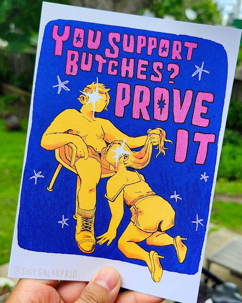 Puede incluir: Una ilustraci&oacute;n azul y amarilla de dos figuras con el texto "YOU SUPPORT BUTCHES? PROVE IT" en rosa. La ilustraci&oacute;n est&aacute; sobre un fondo azul con estrellas blancas.