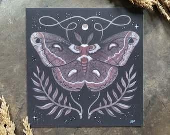 May include: A black and white illustration of a moth with a brown body and white wings. The moth is surrounded by a floral design and a crescent moon. The image is on a black background with white stars.