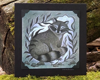 May include: A black and white illustration of a raccoon sitting in a circle of leaves. The raccoon is looking to the right and has a relaxed expression. The illustration is on a black card with a white border.