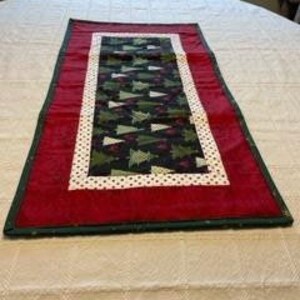 May include: A green and white Christmas tree patterned table runner with a red border and white polka dots.