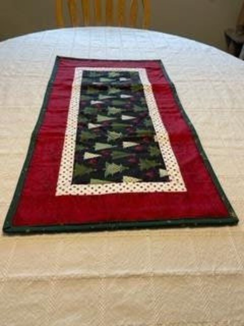 May include: A green and white Christmas tree patterned table runner with a red border and white polka dots.