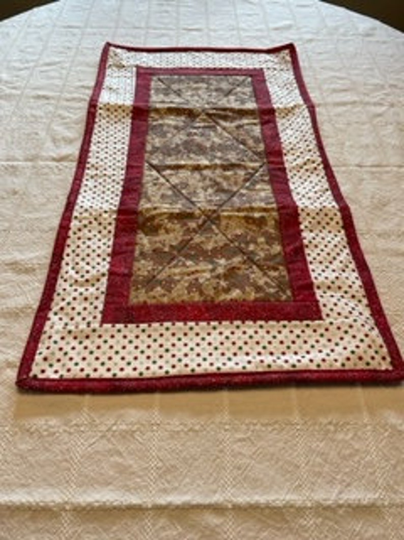 May include: A red and white quilted table runner with a brown and tan patterned centre. The runner has a white background with red polka dots and a red border.