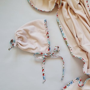 May include: A pale pink swaddle blanket with a floral print border. The blanket is made of soft, breathable fabric and is perfect for keeping baby warm and cozy.