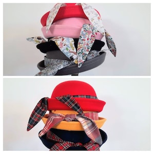 May include: A stack of four hats with different colored felt and patterned fabric bows. The top hat is red, the second is pink, the third is black, and the bottom hat is gray.