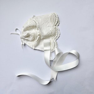 May include: White lace bonnet with a satin ribbon tied in a bow. The bonnet is decorated with delicate embroidery.