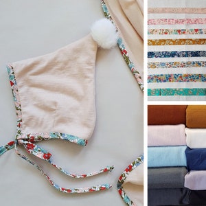 May include: A light pink hooded baby hat with a white pom pom on top. The hat is trimmed with a floral print ribbon. The image also shows a variety of fabrics in different colours and patterns.