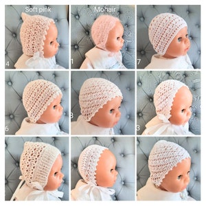 May include: Nine different crocheted baby hats in white and soft pink. The hats are made with a delicate lace pattern and have a pointed top. The hats are displayed on a grey and white patterned fabric.