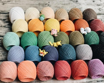 May include: A collection of colorful yarn balls, each with a unique texture and pattern. The yarn balls are arranged in a semi-circle on a wooden surface.