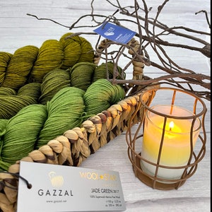 May include: A skein of jade green wool yarn in a wicker basket with a candle in a wire cage. The yarn label reads "Wool Star Jade Green 3817 100% Superwash Merino Fine Wool 100g - 3.52 oz ca. 350m - 382 yd" and "GAZZAL www.gazzal.net"