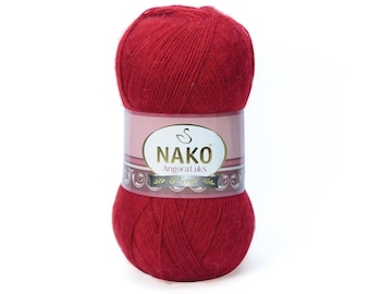 Op de afbeelding: Een bol rode wol met het label "NAKO Angora Luks" op een wit label met de merknaam en een gouden swirl-ontwerp.