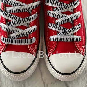May include: Red canvas sneakers with black and white piano key shoelaces. The laces are tied in a criss-cross pattern.