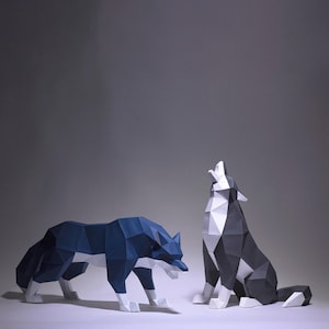 May include: Two origami wolves, one blue and white, the other black and white, are posed against a grey background. The blue and white wolf is lying down, while the black and white wolf is sitting up and howling.