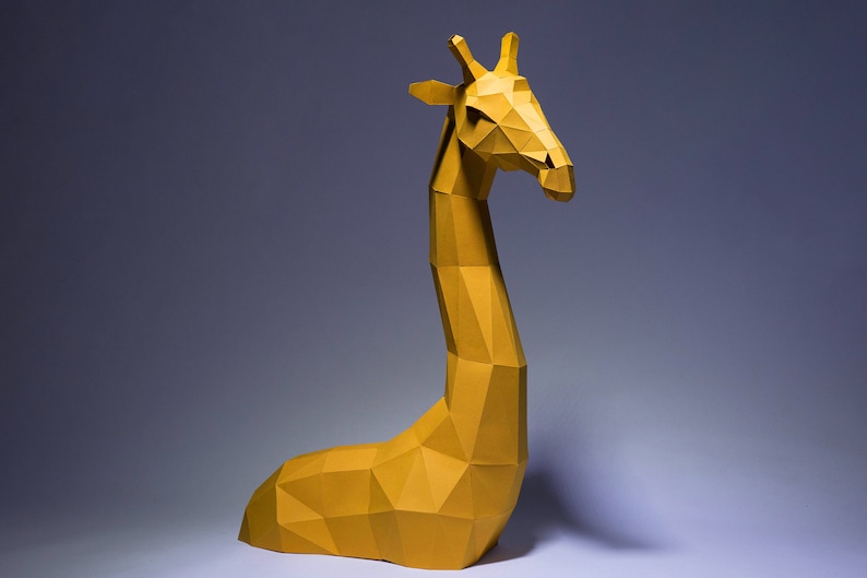 Op de afbeelding: Een gele papieren giraffesculptuur met een geometrisch ontwerp. De giraffe zit met zijn hoofd naar de zijkant gedraaid.