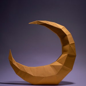 May include: A golden crescent moon sculpture made of paper, with a geometric, origami-style design. The sculpture is on a purple background.