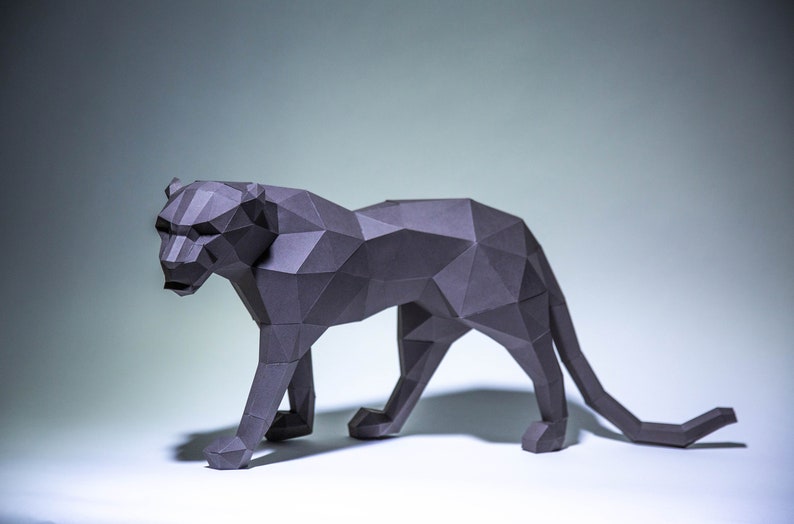 May include: A gray papercraft sculpture of a panther, standing on a white surface. The panther is made of many small triangles, giving it a geometric look.