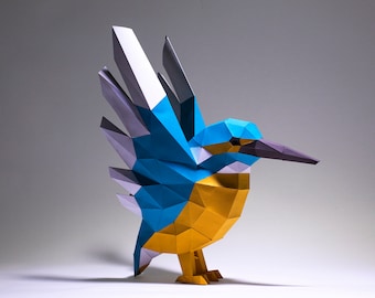 Op de afbeelding: Een blauwe en gele origami ijsvogel met zijn vleugels uitgespreid. De vogel is gemaakt van papier en heeft een gedetailleerd, geometrisch ontwerp.