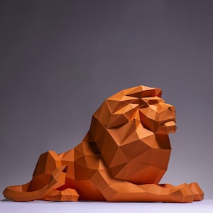 Peut inclure: Une sculpture de lion en origami orange avec un design géométrique. Le lion est couché, la tête tournée sur le côté.
